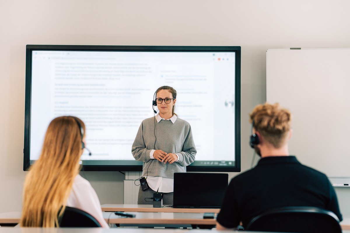 Lehrerin mit Unite-Mikrofon vor Studierenden im Seminarraum